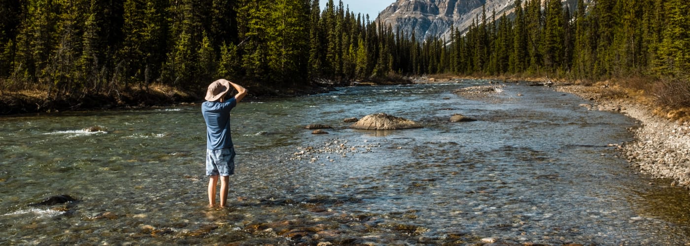 Photograph of a person standing in a stream looking at a mountainscape