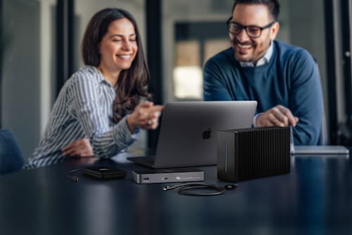 Two people looking at a MacBook Pro on desktop with OWC Thunderbolt 5 Hub and OWC Envoy Ultra
