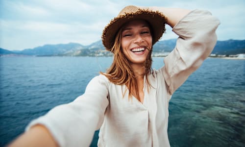 Woman smiling while taking a selfie on the coat of a beach.