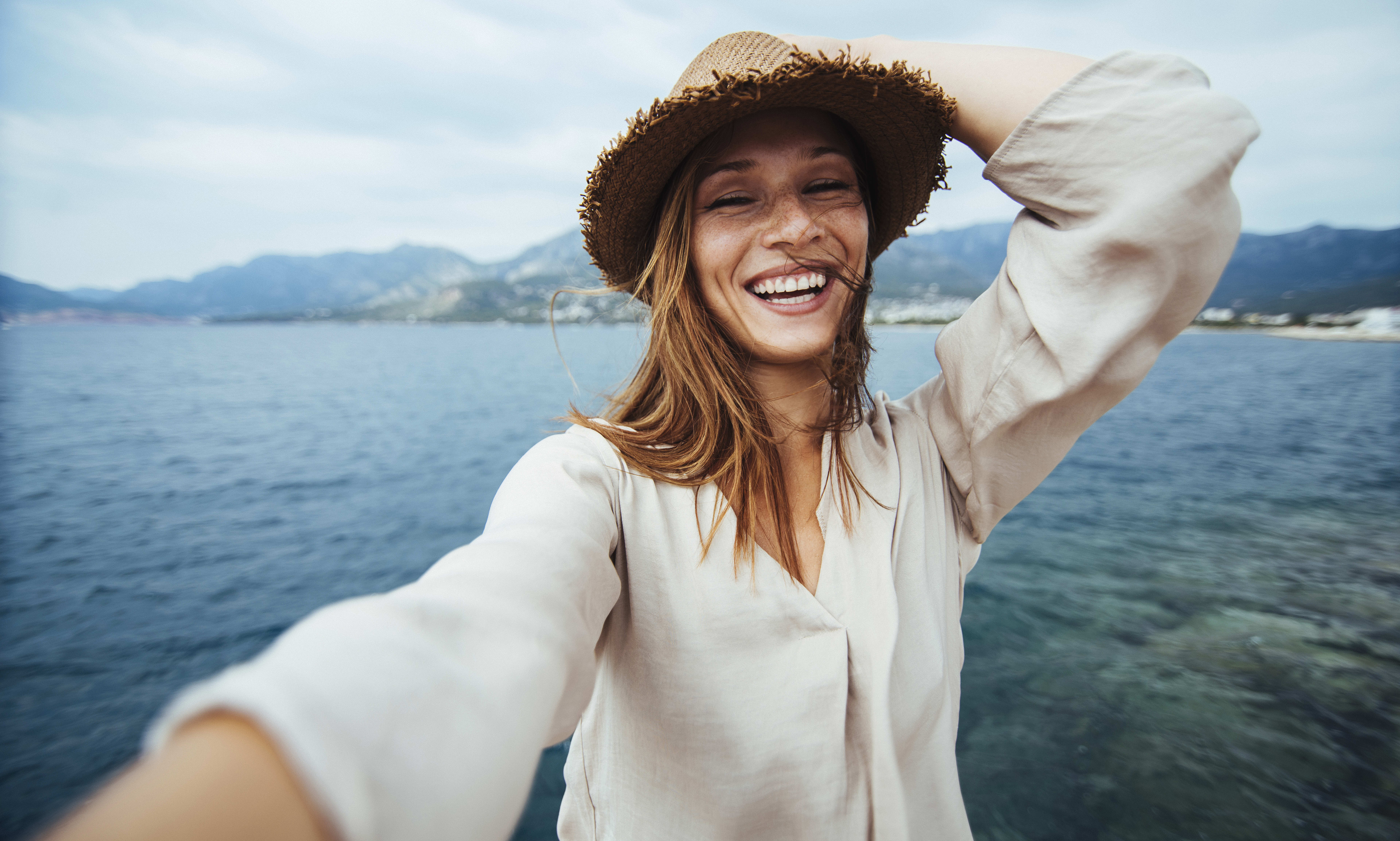 Woman smiling while taking a selfie on the coat of a beach.