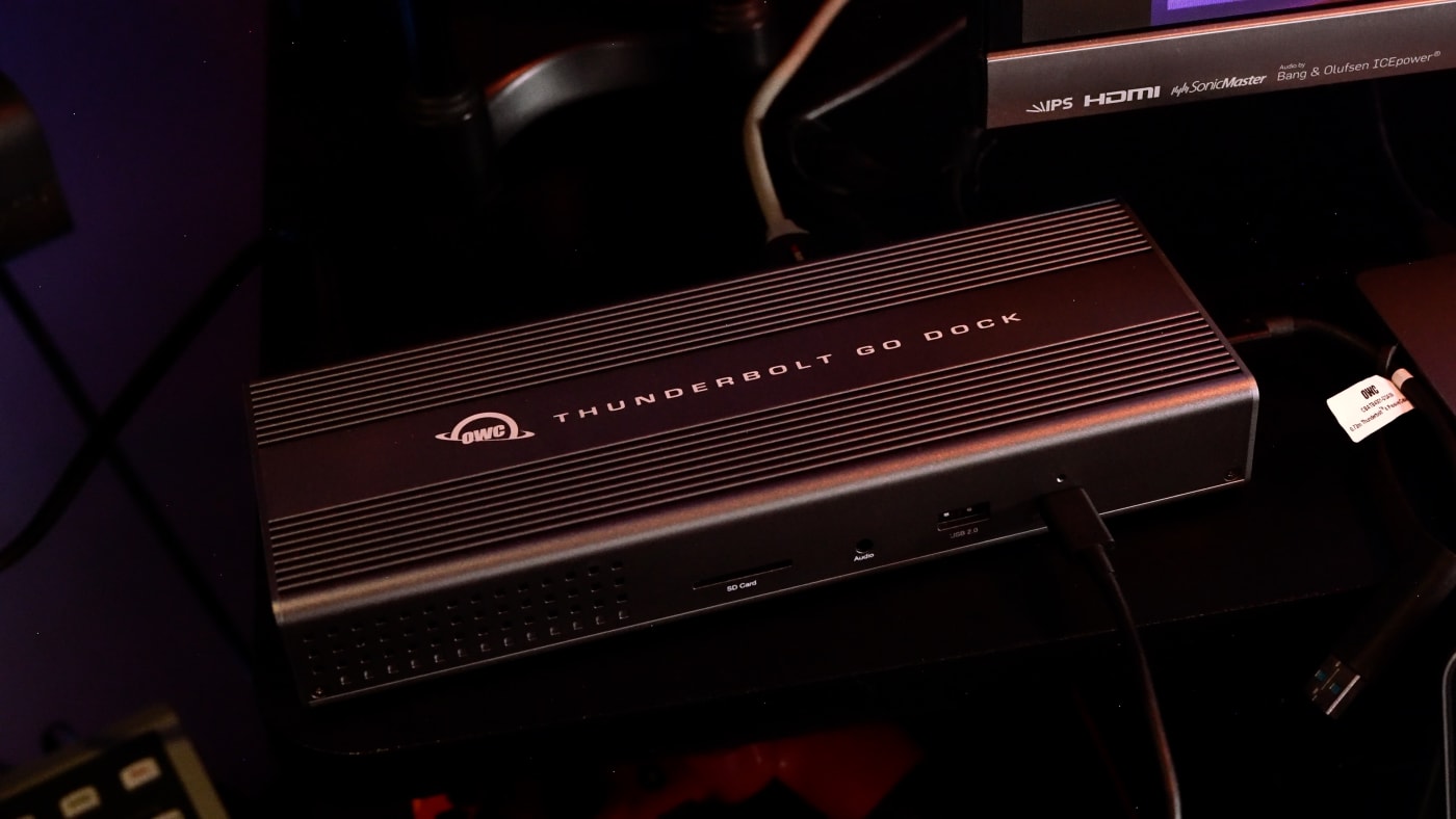 Close-up of an OWC Thunderbolt Go Dock on a desk, connected to a computer setup with various cables and peripherals.