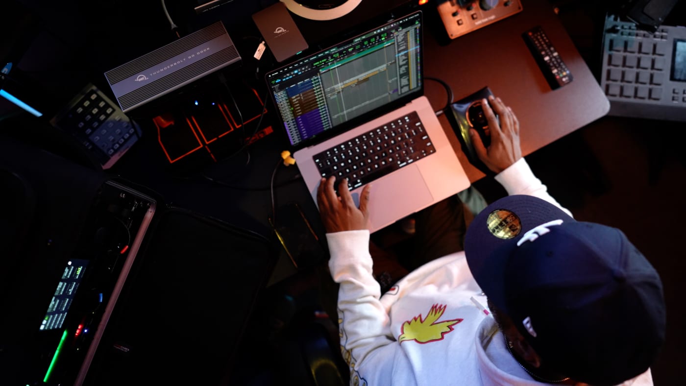 Overhead shot of Adrian Porter working on a laptop in a studio, surrounded by audio equipment including an OWC Thunderbolt 3 dock and external drives.
