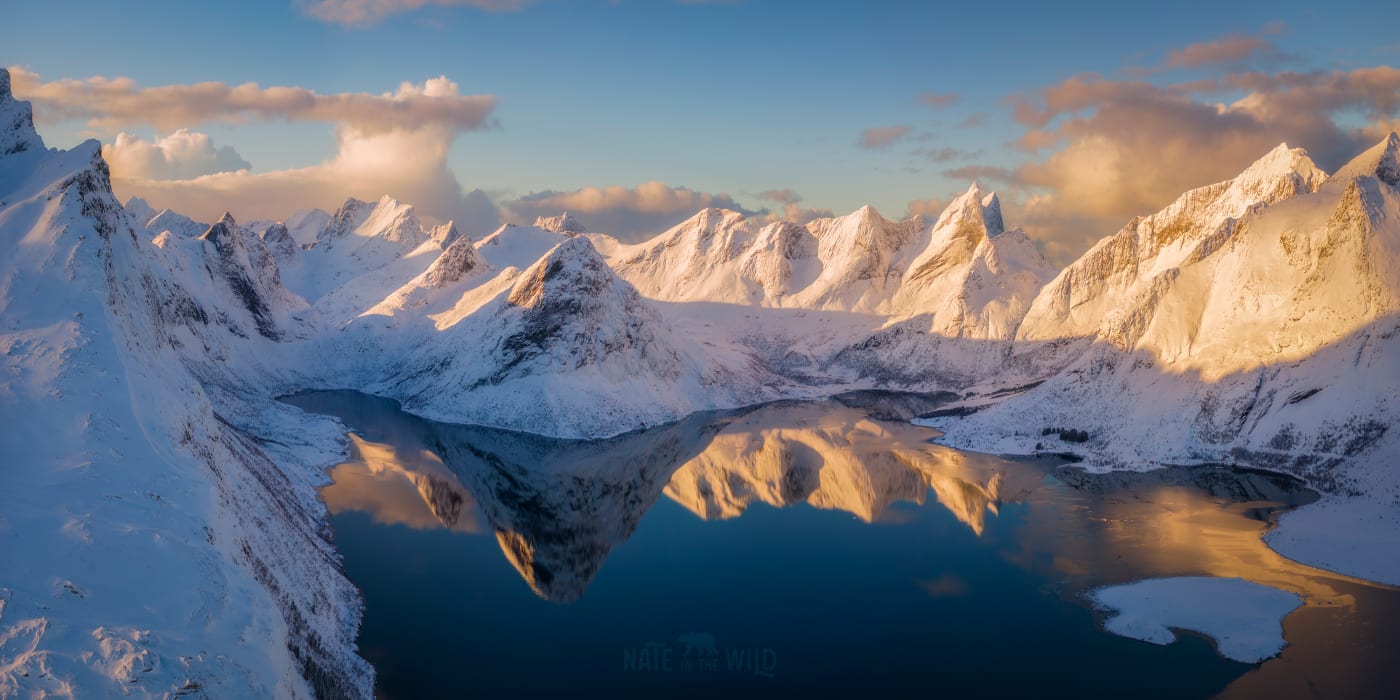 Image of a snow-covered mountain range with sharp peaks reflecting in a calm lake, illuminated by soft sunlight casting shadows across the landscape.