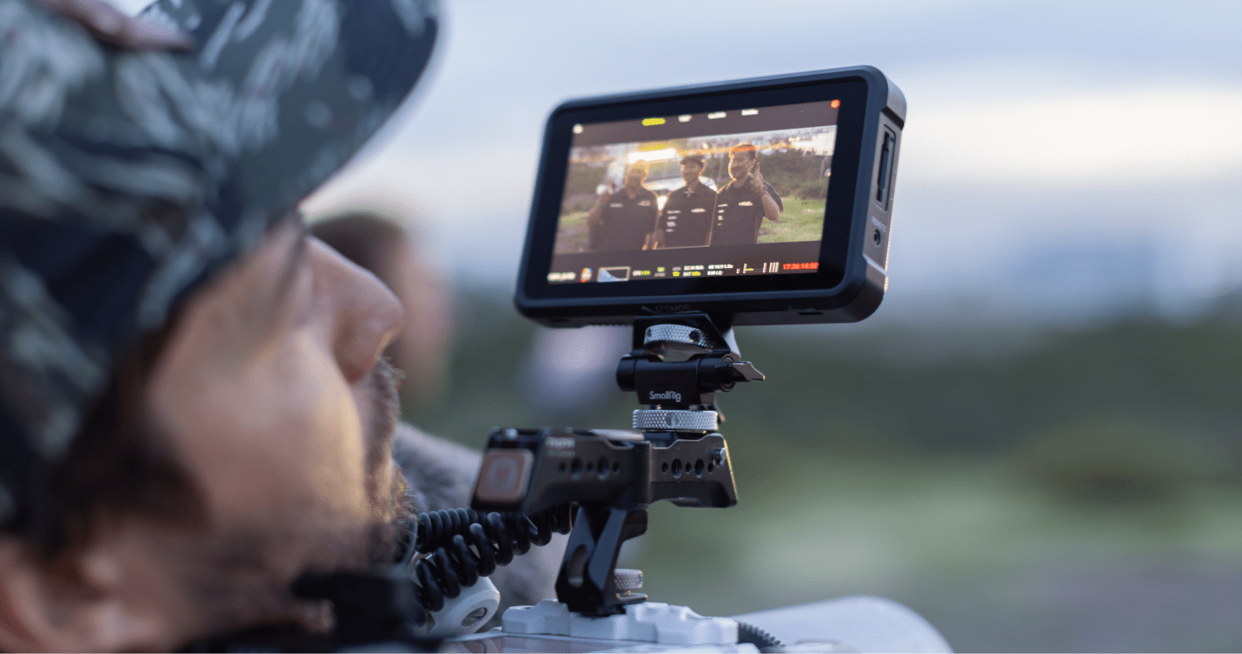 Cahill in the foreground looking at a camera monitor displaying footage of three people, captured during an outdoor shoot.
