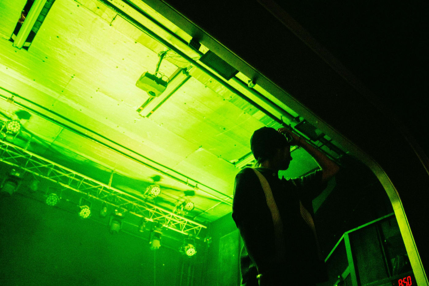 A man stands on a stage with green lighting, silhouetted against a ceiling of beams and lights.