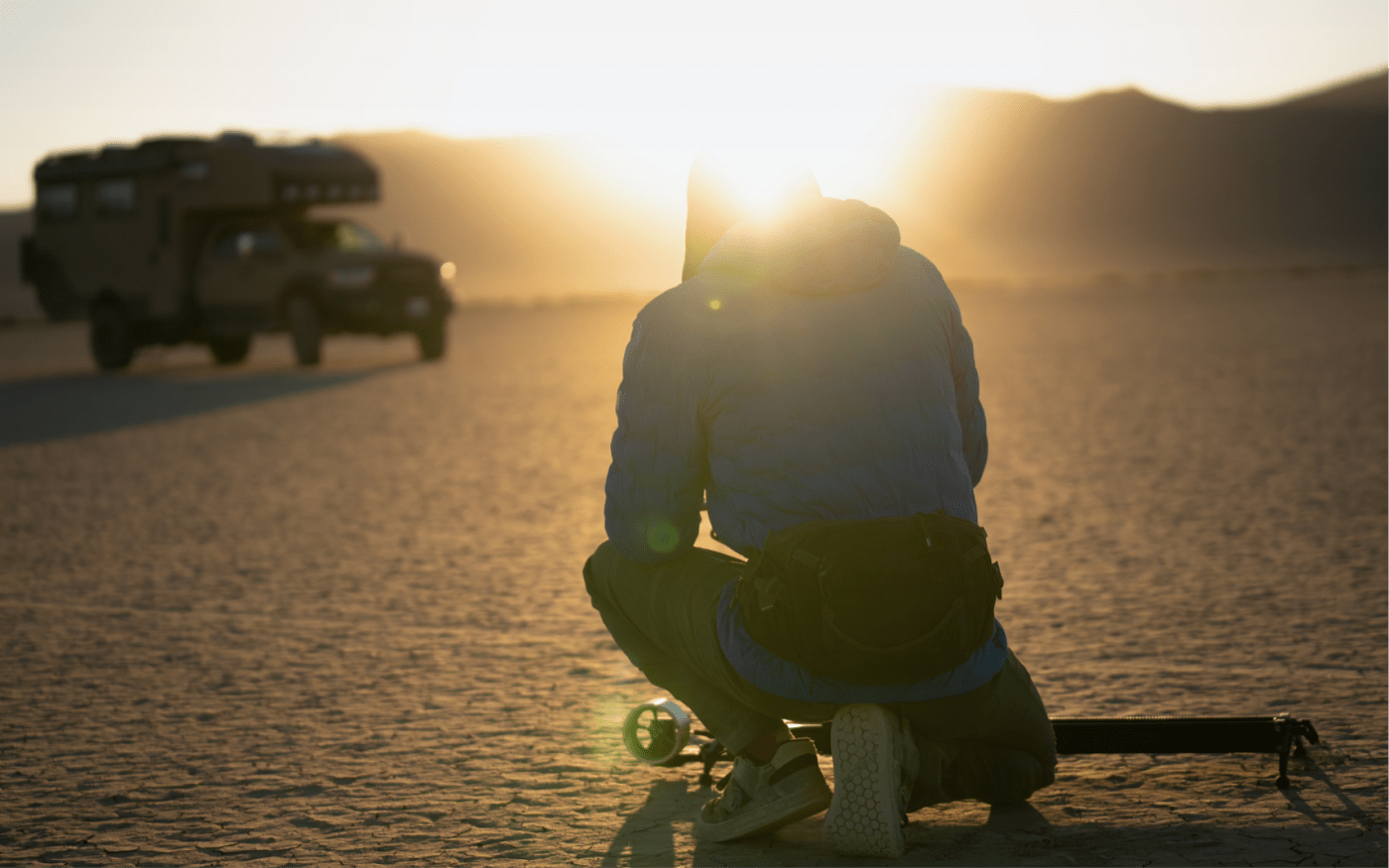 Individual setting up equipment in a desert like landscape with a sun setting in the background