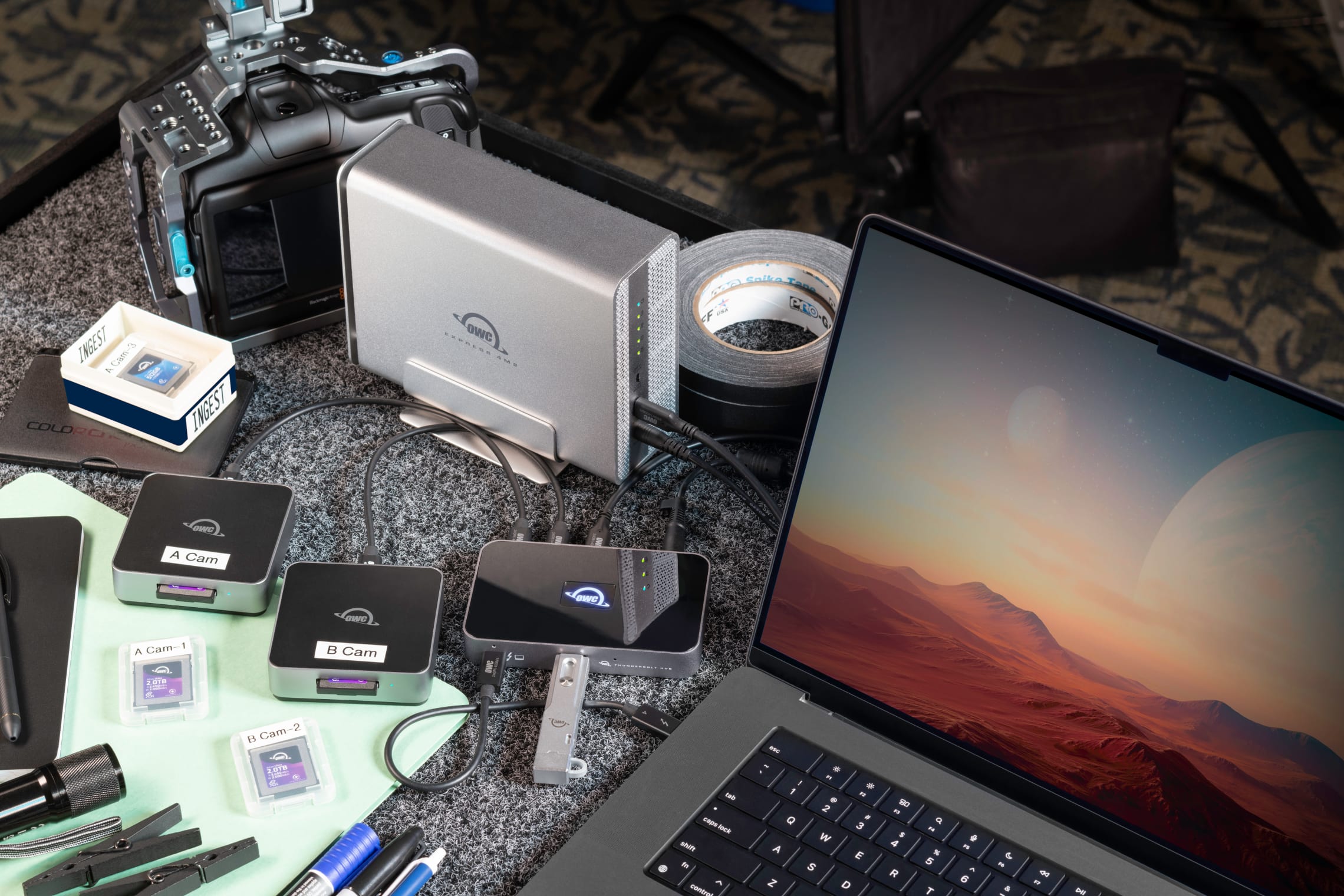 OWC Express 4M2 USB4 NVMe SSD Enclosure connected in a DIT (Digital Imaging Technician) workflow, surrounded by cameras, memory cards, card readers, and a MacBook, emphasizing portable high-speed data ingestion.