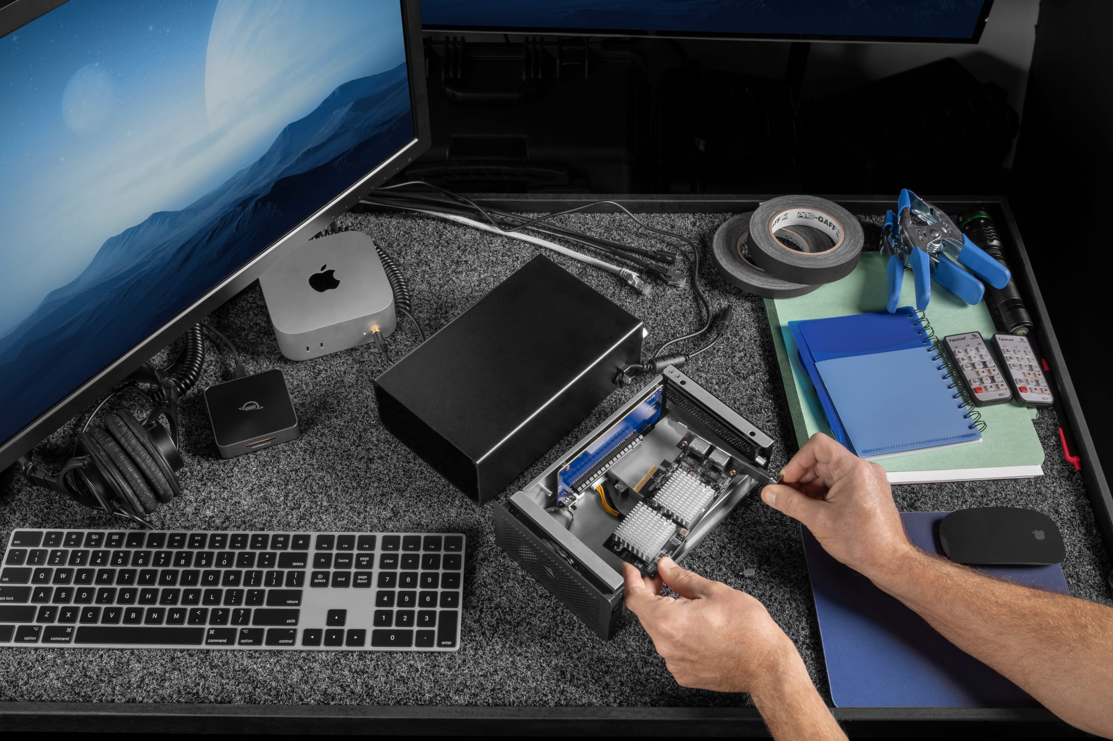 OWC Mercury Helios 5S Thunderbolt 5 PCIe Enclosure laying open atop a workspace, while a professional user is in the midst of installing a new PCIe card.