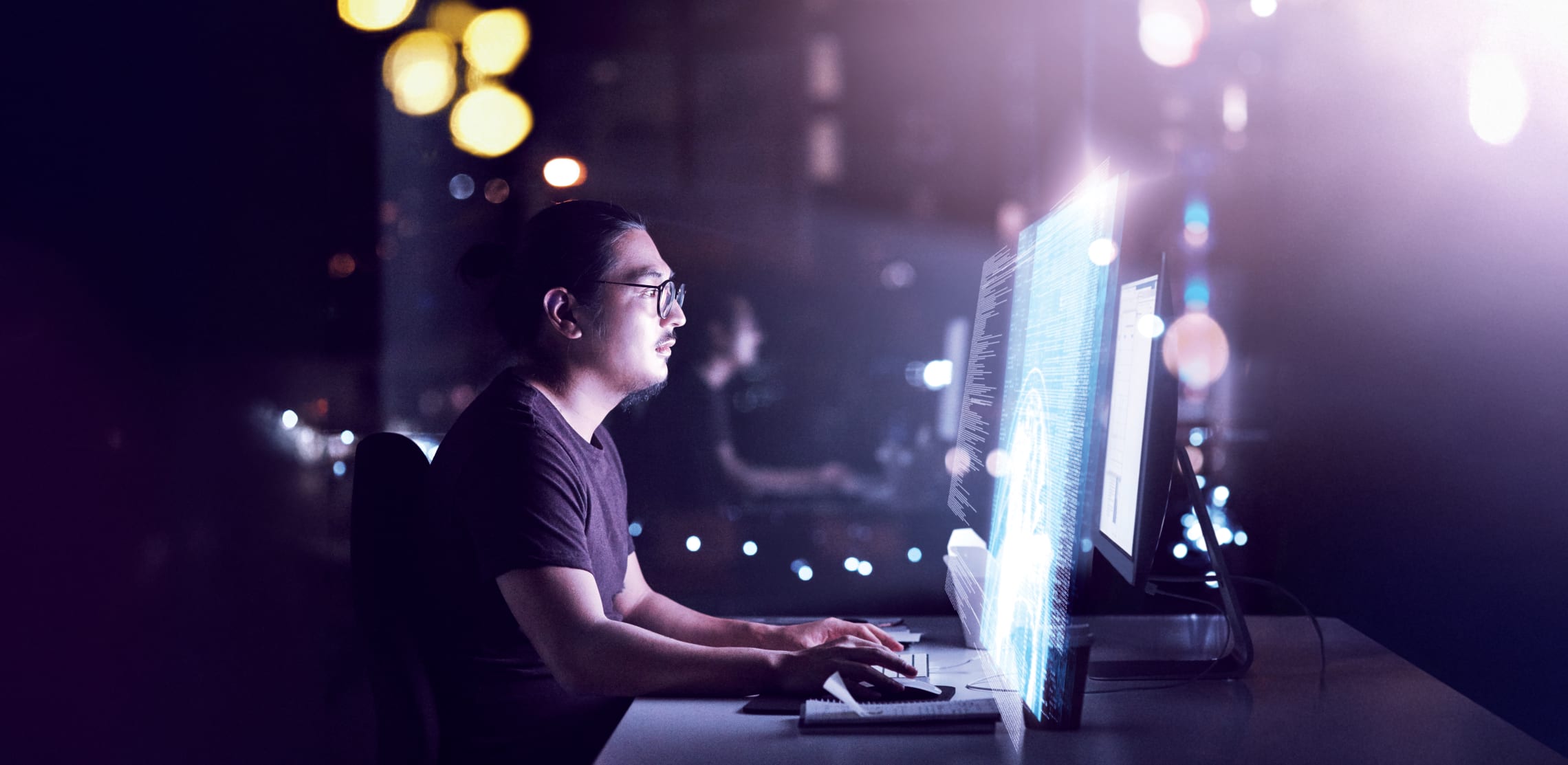 A person working at a computer with code visible on the screen in a dark, tech-focused environment, representing the powerful and professional capabilities supported by the OWC Thunderbolt 5 Hub.