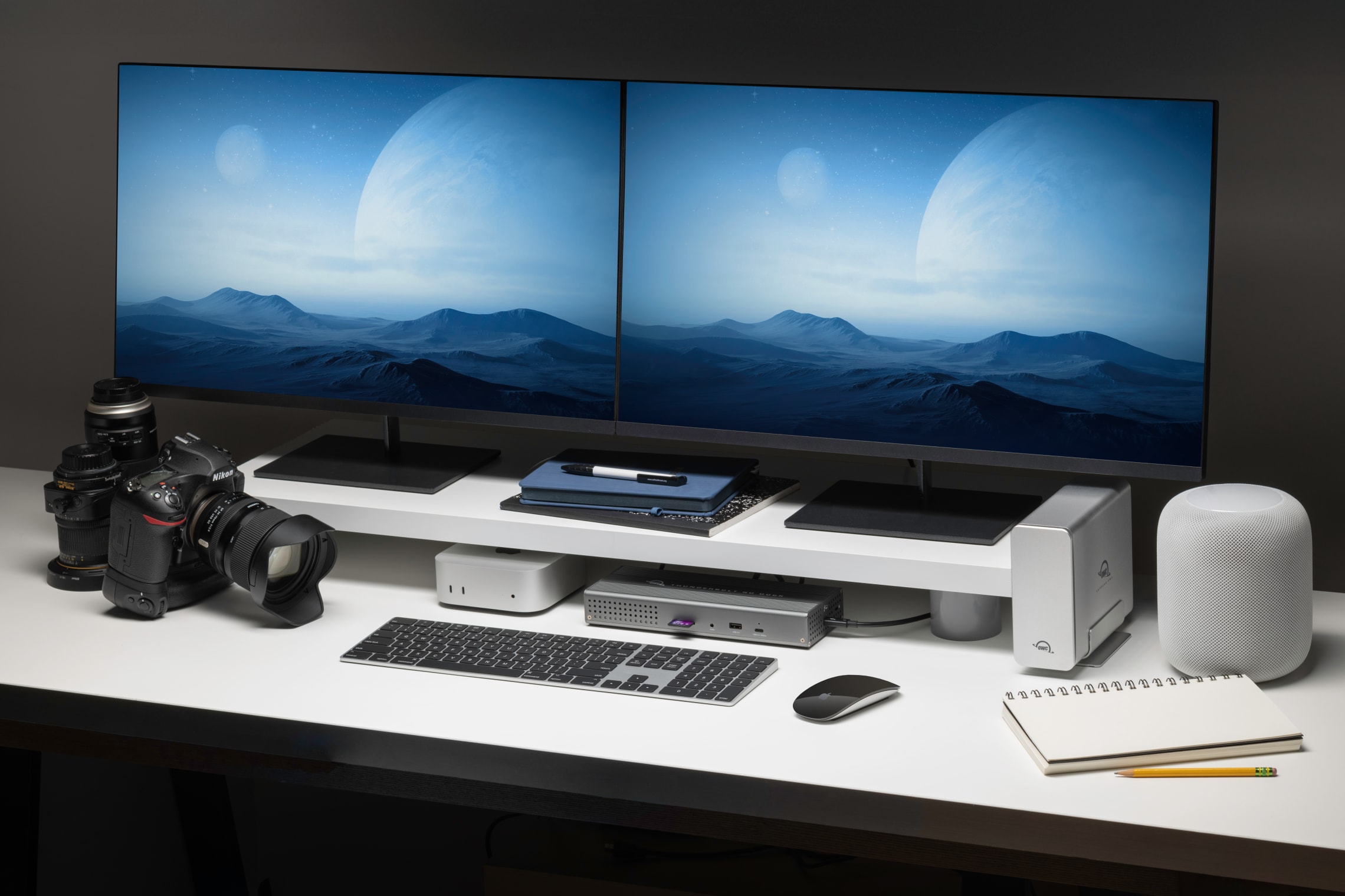 OWC Express 4M2 USB4 NVMe SSD Enclosure featured in a dual-display creative workstation setup with Mac Studio, cameras, accessories, and a clean white desk layout, ideal for photographers and digital creatives.