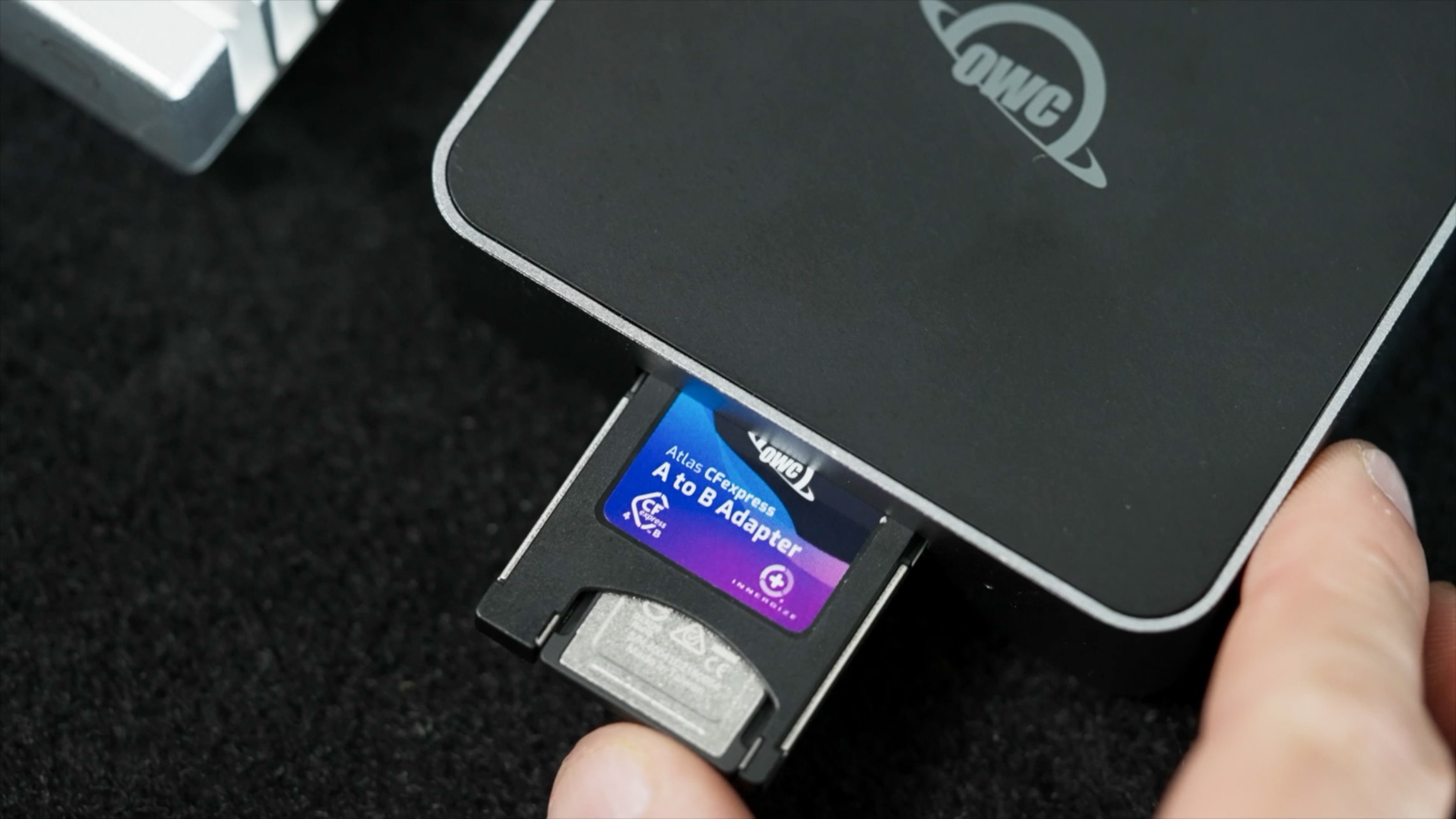 An OWC Atlas CFexpress memory card being inserted into an Atlas A to B adapter, with a close-up of the OWC logo.