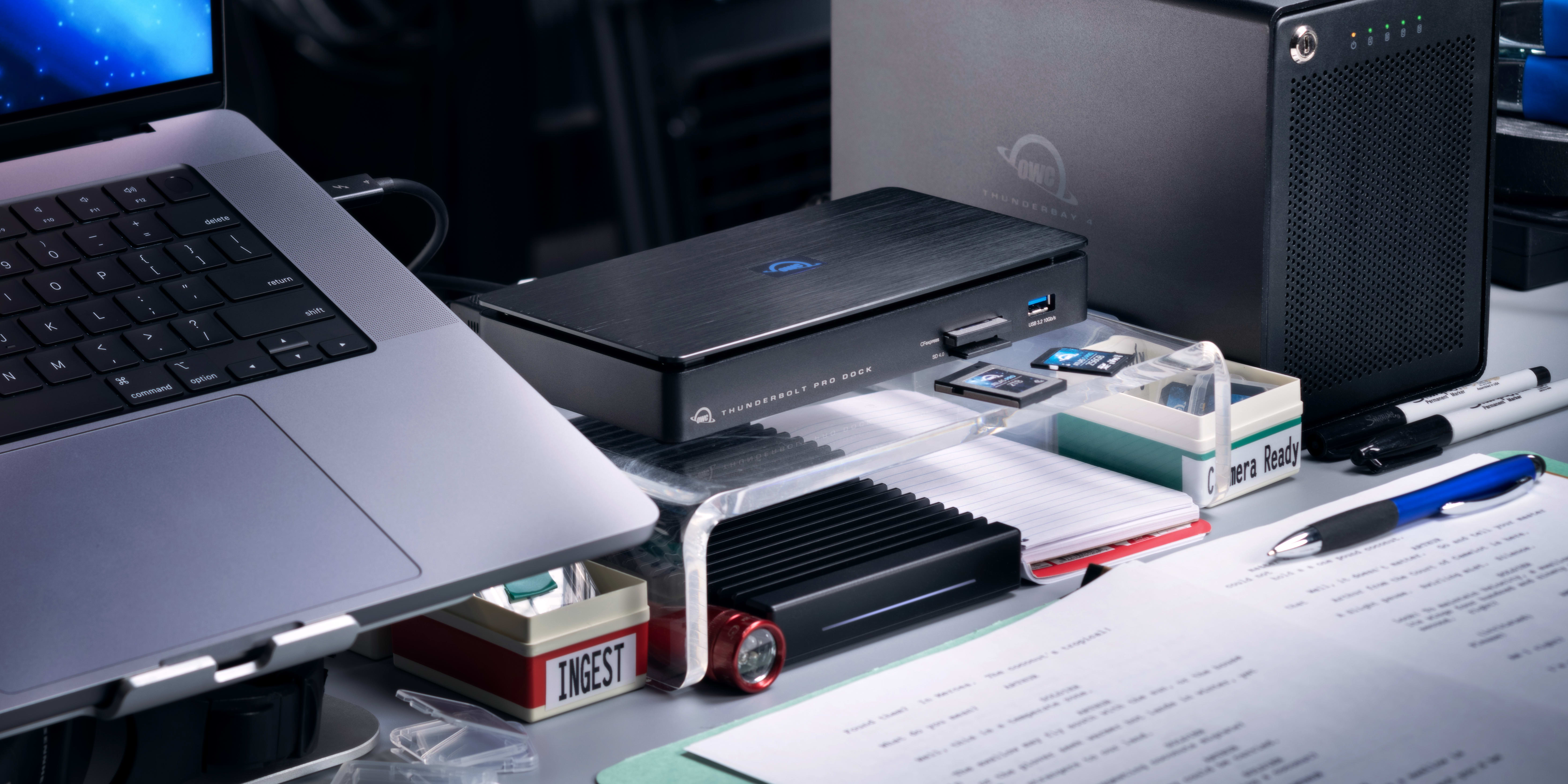An image showing an OWC Thunderbolt Pro Dock on a desk between a laptop and OWC ThunderBay 4 RAID.