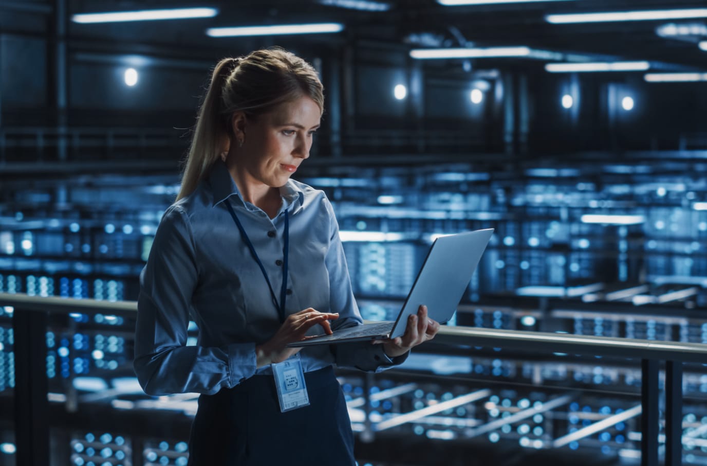 Woman working on a laptop, standing above a server farm